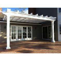 a white pergolated covered patio area with sliding glass doors and brick pavers flooring