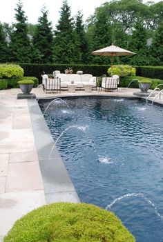 an outdoor swimming pool with lounge chairs and umbrellas in the middle of it, surrounded by greenery