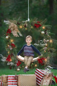 a young boy is sitting on presents in front of a christmas wreath with an ornament