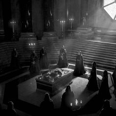 a group of people standing around a casket in a dark room with candles on it