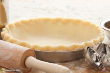 an uncooked pie crust sits next to a rolling pin and other baking supplies