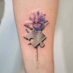 a tattoo with a puzzle piece and flowers on the leg that has a purple flower in it