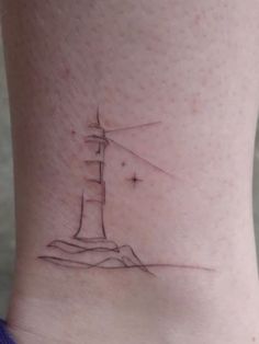 a small lighthouse tattoo on the side of a woman's leg, with stars above it