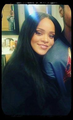 a woman with long black hair smiling at the camera while sitting in front of a mirror