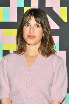 a woman with shoulder length hair standing in front of a colorful background