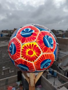 a red and yellow painted ball on top of a wooden stick in front of a cloudy sky