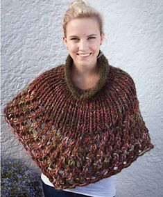 a woman wearing a knitted ponchy standing in front of a white wall