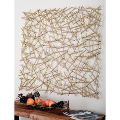 an art piece made out of sticks and fruit on a table next to a wall