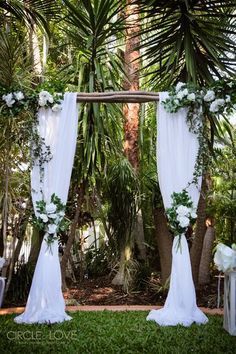 an outdoor ceremony setup with white flowers and greenery on the arbor, surrounded by palm trees