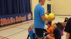 a man holding two yellow balls in his hands while standing on a basketball court with other people