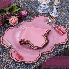 a table set with pink plates, silverware and flowers on the tablecloths