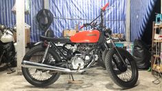 a red motorcycle parked in a garage next to some shelves and other items on the floor