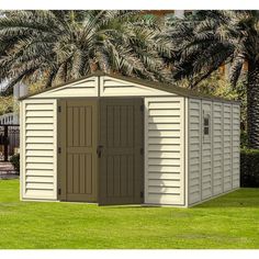 a tan and brown storage shed sitting on top of a green field next to palm trees