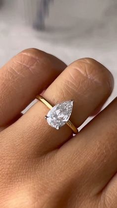 a woman's hand with a yellow gold ring and a pear shaped diamond on it