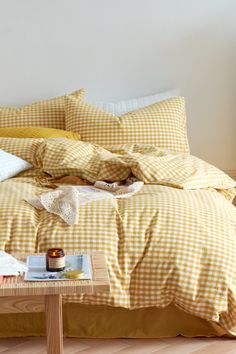 a yellow and white checkered comforter on a bed with pillows, coffee table and lamp