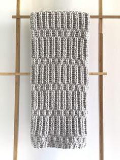 a gray and white knitted dishcloth hanging on a wooden rack in front of a wall