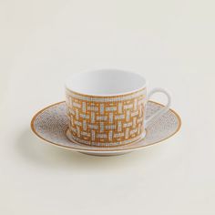 a cup and saucer on a white surface with an orange pattern in the middle