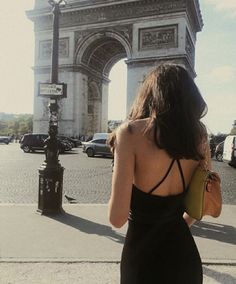 a woman in a black dress is looking at the arc de trioe triumph gate