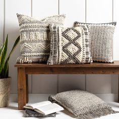 three pillows and a book on a bench with a potted plant in the corner