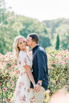 a man and woman standing next to each other in front of some bushes with flowers