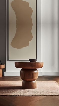 an abstract art piece is displayed on the wall above a round wooden table in front of a window