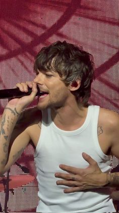 a male in a white tank top singing into a microphone and holding his hands out