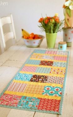 a wooden table topped with a colorful rug next to two vases filled with flowers