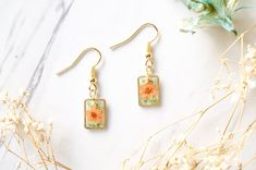 a pair of earrings sitting on top of a table next to dried flowers and leaves