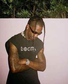 a man with dreadlocks standing in front of a white wall wearing a black t - shirt