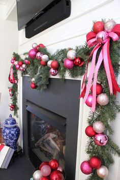 a fireplace decorated for christmas with red, silver and pink ornaments on the mantel