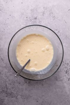 a glass bowl filled with liquid on top of a gray counter next to a spoon