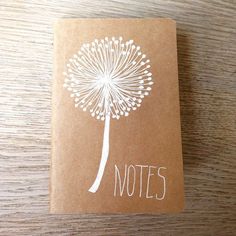 a notepad with a dandelion drawn on it sitting on top of a wooden table