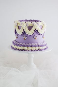 a purple and white cake sitting on top of a white cake plate with ruffles