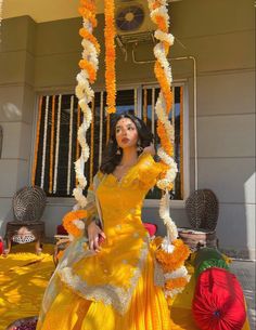 a woman in a yellow dress is standing under an orange and white umbrella with flowers hanging from it