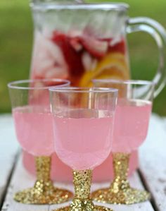 pink and gold glasses are sitting on a wooden table with a pitcher in the background