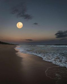 the full moon is setting over the ocean and beach with waves coming in to shore