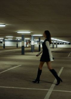 a woman is walking in an empty parking lot with her legs crossed and black boots on