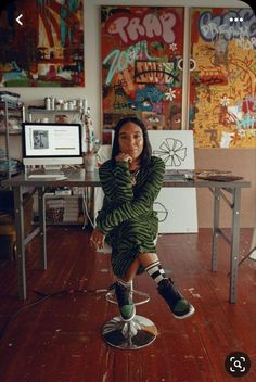 a woman sitting on top of a metal stool in front of a desk with computer monitors