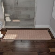 a bath room with a toilet and a rug on the floor in front of a shower