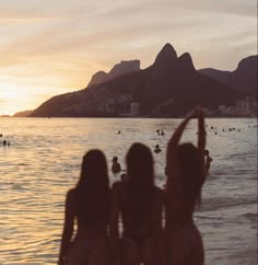 three women standing in the water at sunset with mountains in the background