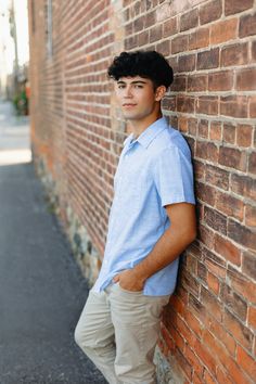 a young man leaning against a brick wall