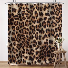 a leopard print shower curtain hanging on a wall next to a stool and vase with flowers