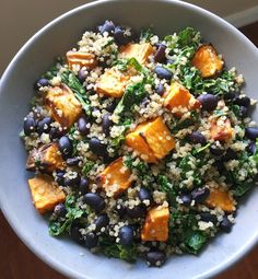 a white bowl filled with black beans, rice and greens on top of a wooden table