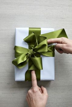 a person pointing at a present wrapped in green satine with a bow on it