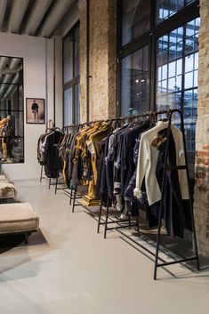 a clothing store with clothes hanging on racks and benches in front of the glass windows