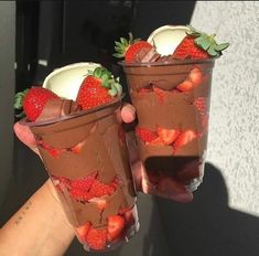 two cups filled with chocolate and strawberries on top of each other, one being held up by someone's hand