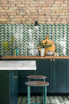 a kitchen with green cabinets and white counter tops, along with a brick wall behind it