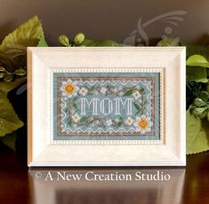 a cross stitch pattern with the word mom on it in a frame next to some flowers