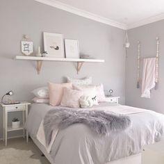 a white and gray bedroom with some pink pillows on the bed, two shelves above the bed