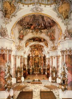 an ornately decorated church with pews and paintings on the walls